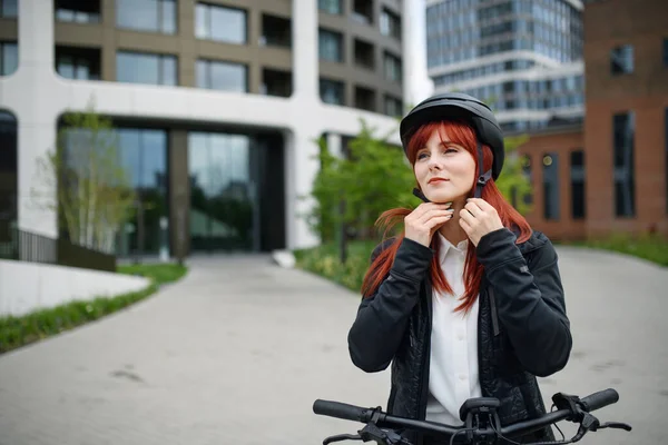 A portrait of businesswoman commuter on the way to work putting on cycling helmet, sustainable lifestyle concept.