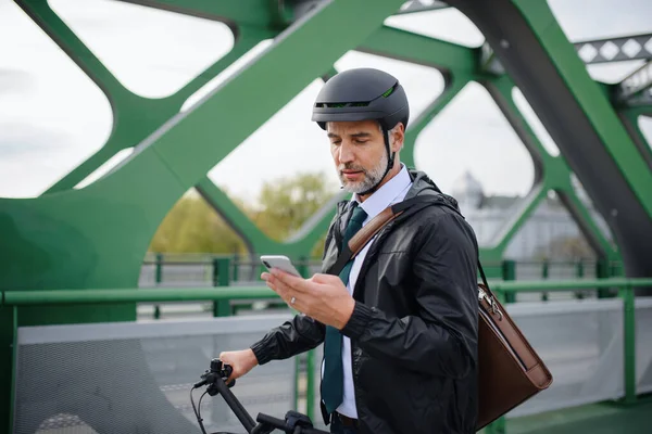 A businessman commuter on the way to work, pushing bike on bridge and texting on mobile phone, sustainable lifestyle concept.