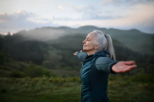一位老年妇女在大自然中做呼吸运动 背景是大雾和群山 — 图库照片
