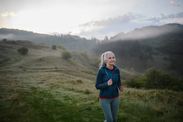 Starsza Kobieta Jogging Przyrodzie Wczesnym Rankiem Mgłą Górami Tle — Zdjęcie stockowe