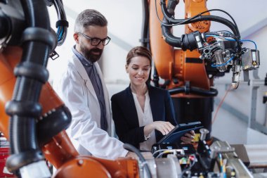 Robot mühendisleri bir tabletle fabrikada modern robotik kolu dikte ediyor ve söküyor..