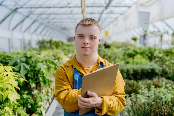 Młody Człowiek Zespołem Downa Pracujący Centrum Ogrodnictwa Podkładce Sprawdzający Rośliny — Zdjęcie stockowe