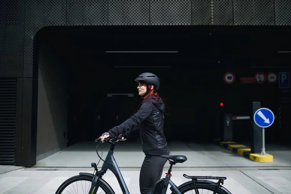 A portrait of businesswoman commuter on the way to work with bike looking at camera, sustainable lifestyle concept.