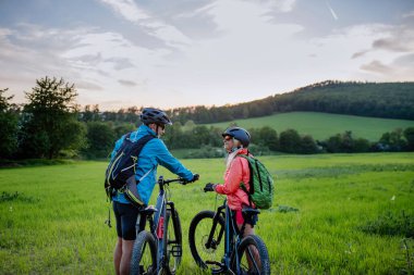 Aktif bir son sınıf çifti yaz parkında çimlerin üzerinde bisiklet sürüyor. Sağlıklı yaşam tarzı kavramı..