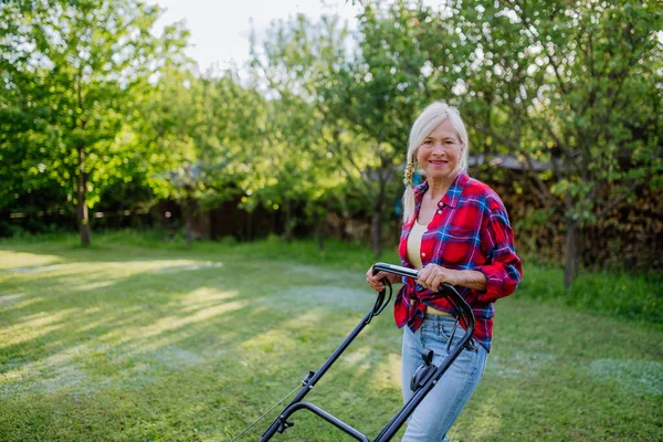 庭の芝刈り機で草を刈る年配の女性 庭の仕事の概念 — ストック写真