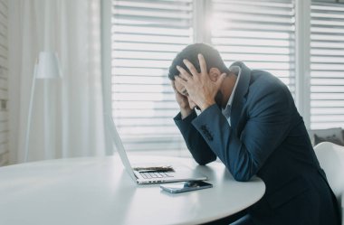 Depresyonda olan bir işadamı ofis masasında bilgisayarla çalışarak avro parası sayıyor, enflasyon kavramı.
