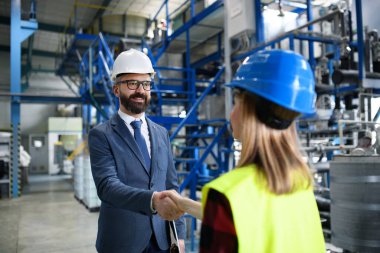 Üniformalı bir mühendis ve sanayi işçisi büyük bir metal fabrikasında el sıkışıyor ve konuşuyor..