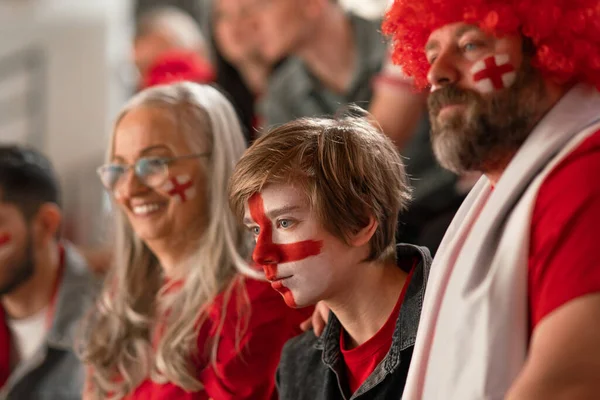 Excited football fans supproting an English national team in live soccer match at stadium.