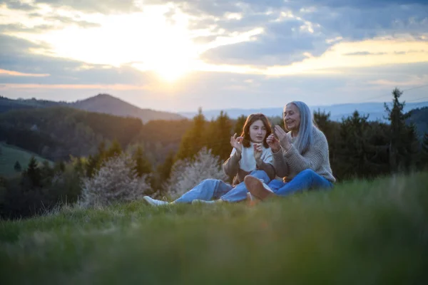 Uma Avó Sênior Feliz Com Granddaguhter Adolescente Sentado Assobiando Grama — Fotografia de Stock