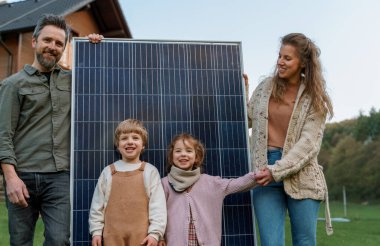 Evlerinin yakınında güneş panelleri olan mutlu bir aile. Alternatif enerji kaynağı