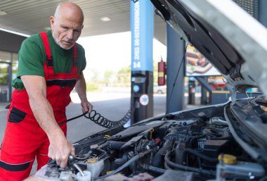 Kıdemli bir tamirci araba motorundaki yağ seviyesini kontrol ediyor..