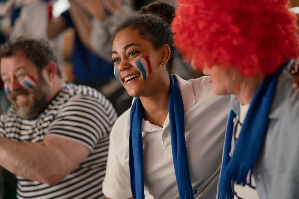 Excited football fans supproting French national team in live soccer match at a stadium.