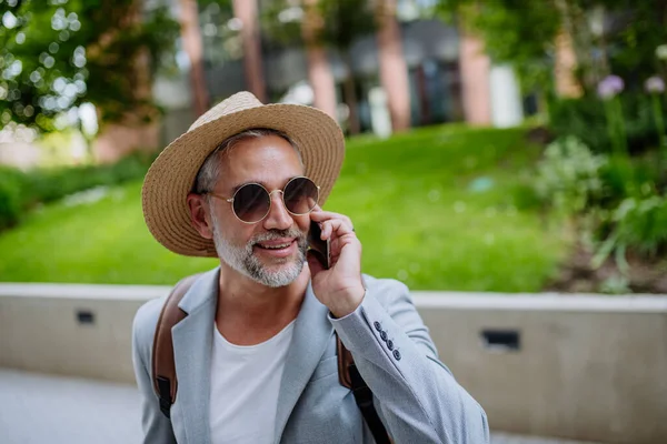仕事の途中で夏にカジュアルな服を着たビジネスマン 電話で話しているわら帽子とバックパックを身に着けている自信のある男 — ストック写真