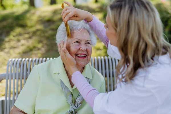 Caregiver Helping Senior Woman Comb Hair Make Hairstyle Sitting Bench — Stockfoto