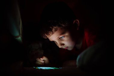 Geceleri telefonda oyun oynayan bağımlı küçük bir çocuk..