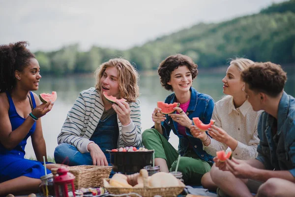 湖の近くのピクニックを楽しみ 毛布に座ってスイカを食べる若い友人のグループ — ストック写真