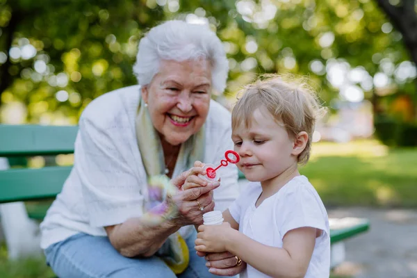 Una Bisnonna Seduta Sulla Panchina Con Sua Nipote Soffiando Bolle — Foto Stock