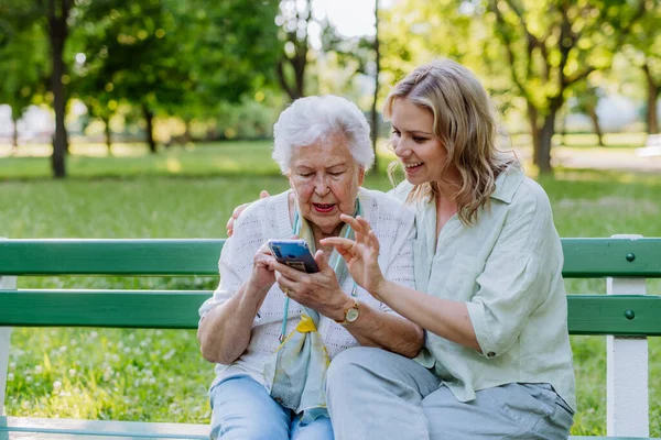Egy Felnőtt Nagypapa Segít Nagyanyjának Mobilt Használni Amikor Nyáron Padon — Stock Fotó