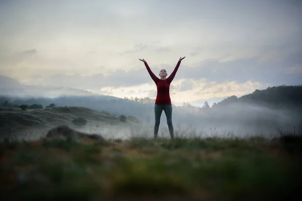 霧と山を背景に早朝に自然の中で呼吸運動をしている上級女性 — ストック写真