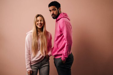 Pembe arka planda poz veren kapüşonlu mutlu sarışın bir kadının moda stüdyosu portresi..