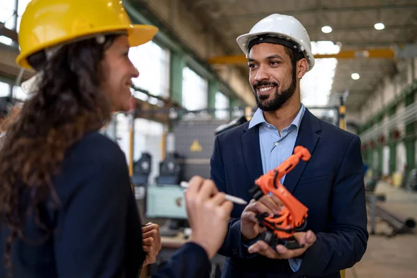 一位持有工业机械臂模型并在工厂向同事展示的男性工程师 — 图库照片
