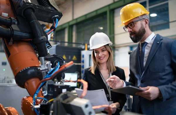 A chief engineer and project manager in modern industrial factory with robot arms talking and planning optimization of production.