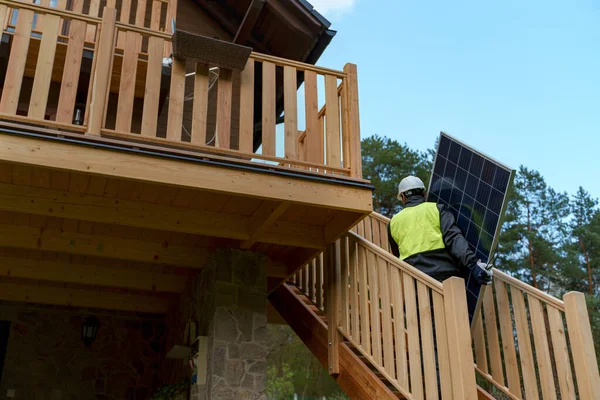 家の上に太陽光発電システムをインストールするための太陽電池パネルを運ぶ男の労働者 — ストック写真
