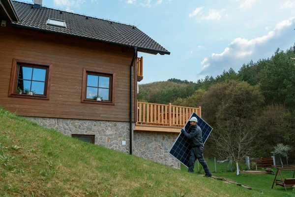家の上に太陽光発電システムをインストールするための太陽電池パネルを運ぶ男の労働者 — ストック写真