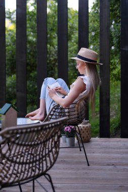 Genç ve güzel bir kadın rahat bir terasta rahatlıyor, kitap okuyor, dijital detoks yapıyor ve hafta sonu kaçamağı kavramını anlatıyor..