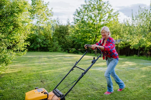 庭の芝刈り機で草を刈る年配の女性 庭の仕事の概念 — ストック写真