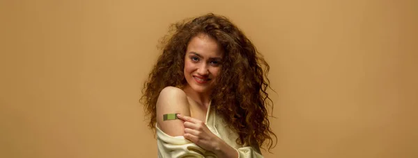 ワクチンを飲んだ女性の笑顔が描かれている 黄色の背景に隔離されたワクチン接種を受けた後 彼女のシャツの袖を保持し 包帯で彼女の腕を示し女性 — ストック写真