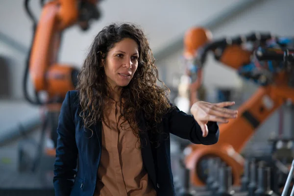An automation female engineer talking to somebody about programming robotic arm in factory.