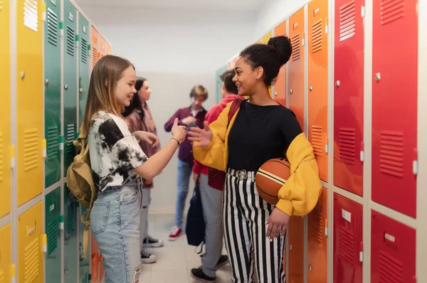 Young high school students meeting and greeting near locker in a campus hallway, back to school concept.