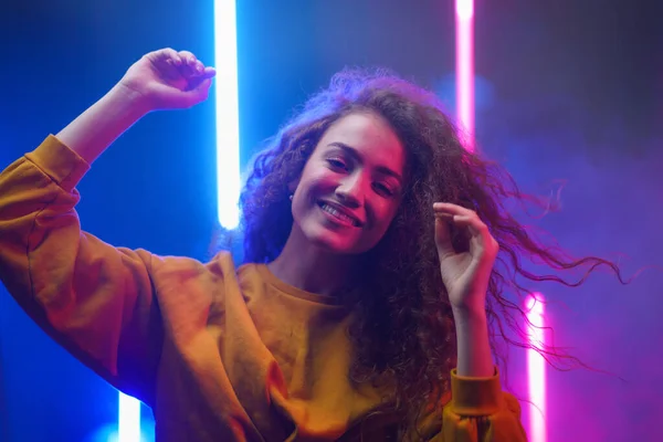A portrait of a happy young woman dancing over neon light background at disco party