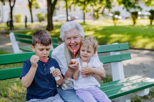 一位曾祖母和她的孙子孙女坐在长椅上 一起吹肥皂泡 代代相传 — 图库照片
