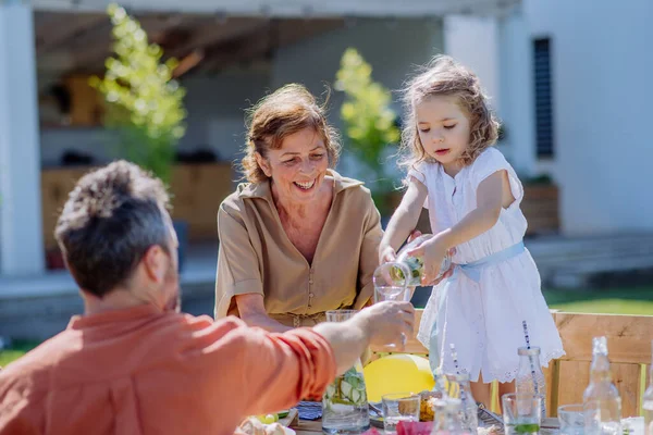 一个代代相传的家庭正在举行花园派对庆祝活动 小女孩正在给她的父亲浇果汁 — 图库照片