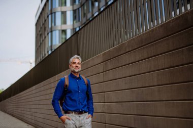 Sırt çantalı bir adam sokakta yürüyor, iş adamı yazın işe giderken günlük giysiler giyiyor..