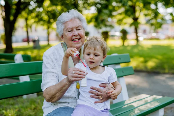 一位曾祖母和孙女坐在长椅上 一起吹肥皂泡 代代相传 — 图库照片