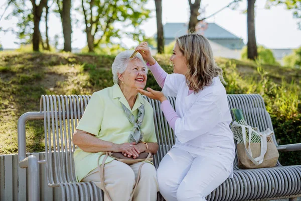 一位看护者在公园的长椅上帮助老年妇女梳头 做发型 — 图库照片