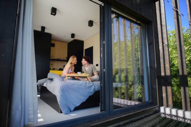 Genç ve güzel bir çift yatakta oturup sağlıklı bir kahvaltı yapıyor..