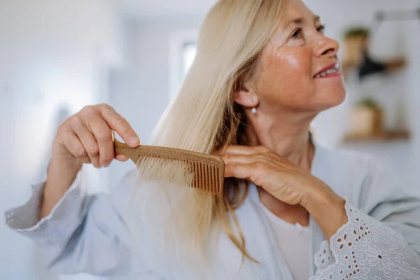 一位穿着浴衣的漂亮老年女士在浴室里用木制梳子梳理头发 可持续的生活方式 — 图库照片