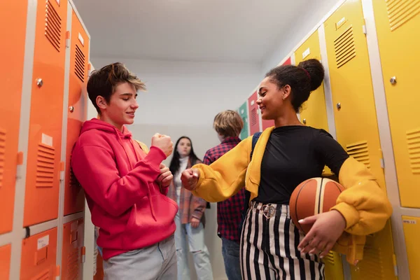 Young high school students meeting and greeting near a locker in campus hallway talking and high fiving.