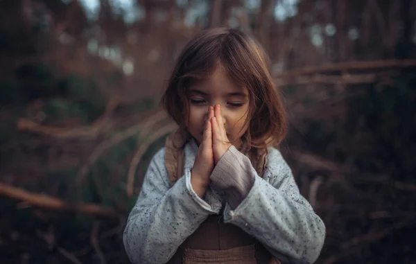 A happy little girl with closed eyes praying in autumn forest.