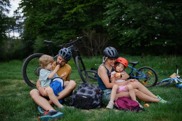 一个有小孩的年轻家庭骑自行车后休息 夏天坐在公园的草地上 — 图库照片