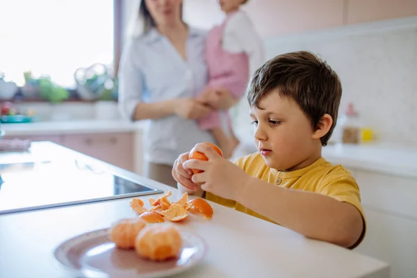 Little Boy Peeling Tangerine Him His Little Sister Mother Background — Stock fotografie