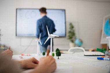 Bir grup son sınıf öğrencisi sınıfta öğretmenle karşılıklı enerjiyi tartışıyor, model rüzgar türbininin yakın plan görüntüleri..