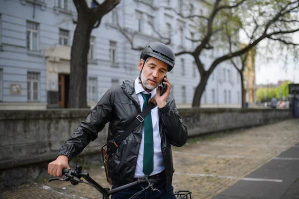 A portrait of businessman commuter on the way to work, pushing bike and calling on mobile phone, sustainable lifestyle concept.