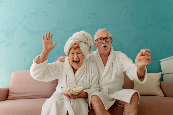 Happy Senior Couple Sitting Sofa Bathrobes Watching Popcorn — Stock Fotó