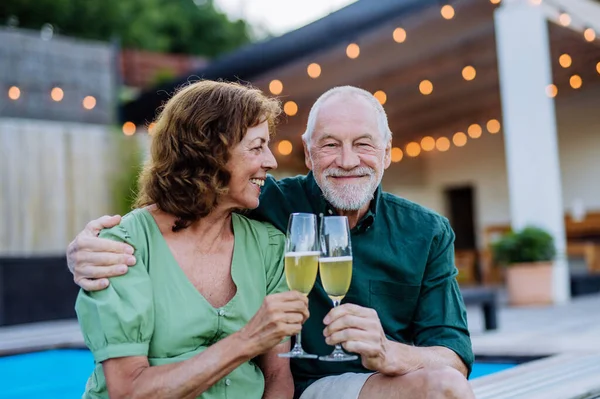 A man with his wife celebrating birthday and toasting with wine near backyard pool.