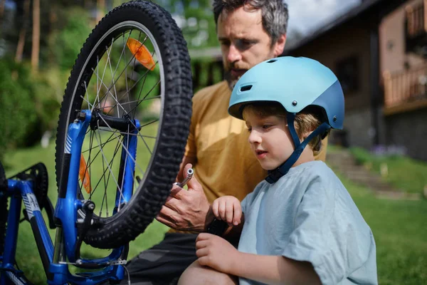 家の前の庭でタイヤを汲み上げ自転車に乗る準備を一緒に小さな息子を持つ父親 — ストック写真
